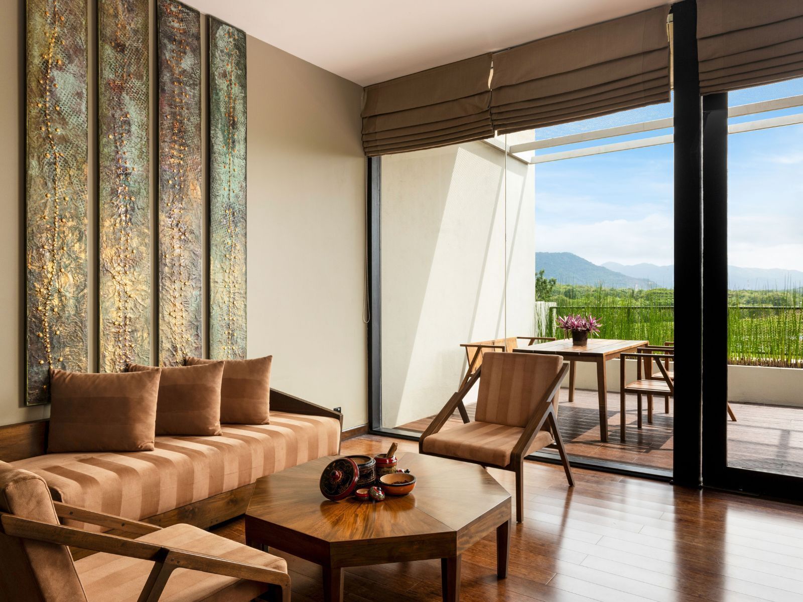Una sala de estar moderna con un sofá, sillas, una mesa de centro y vistas a un paisaje verde a través de grandes ventanales.