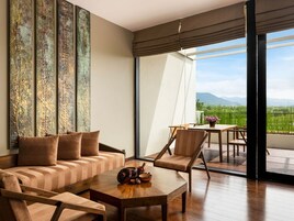 Una sala de estar moderna con un sofá, sillas, una mesa de centro y vistas a un paisaje verde a través de grandes ventanales.