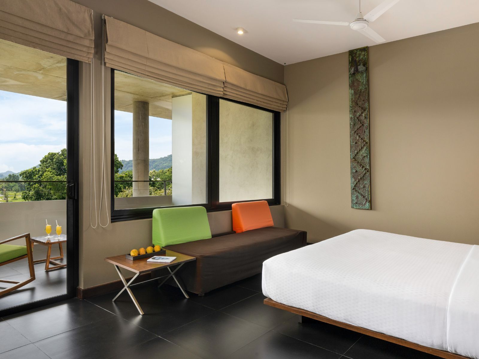 Habitación de hotel moderna con una cama grande, una mesita con una silla, un sofá y vistas al exterior.