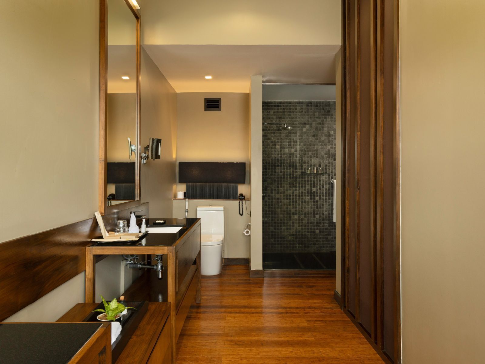 A modern bathroom with a wooden vanity, a large mirror, a shower with mosaic tiles, and a white toilet.