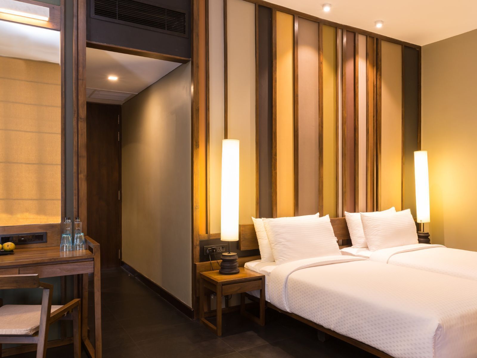 A hotel room with a bed, bedside tables, a desk, and a mirror.