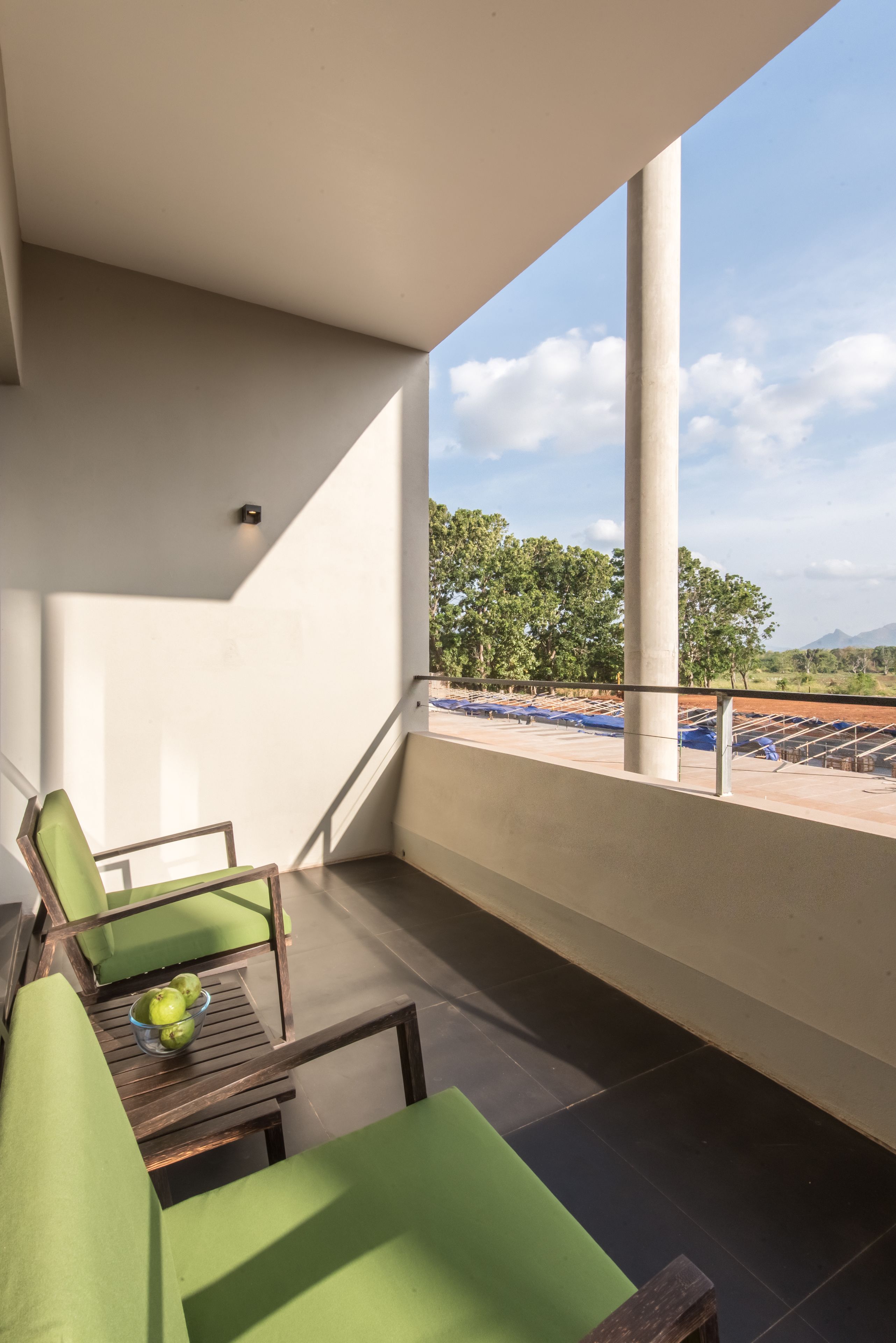 Un balcón con asientos acolchados verdes, una pequeña mesa con un cuenco de fruta y vistas a árboles y un paisaje lejano.