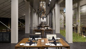 A modern dining area with wooden tables and chairs, a central hanging light fixture, and a view of the outdoors.