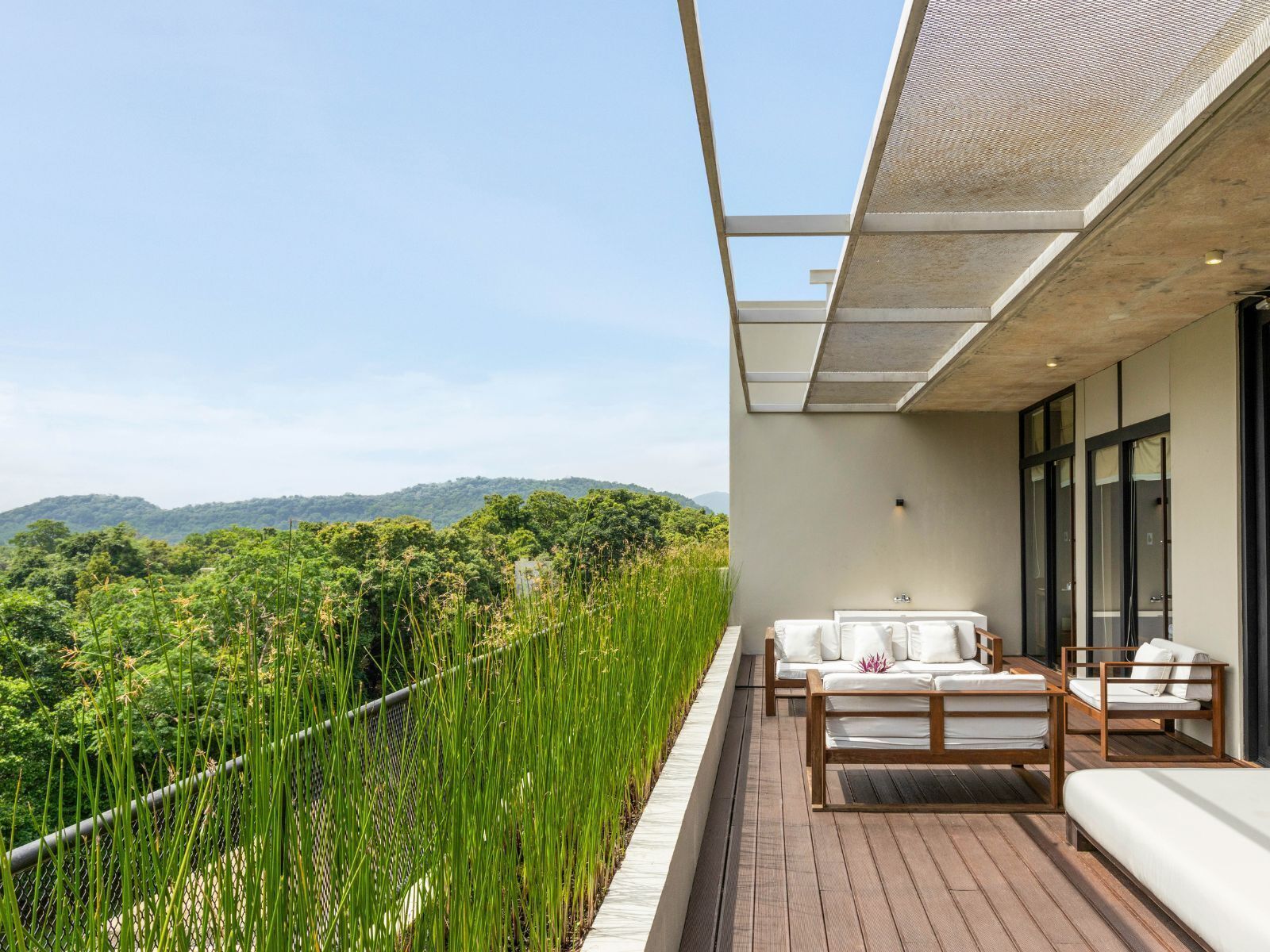 A balcony with a wooden floor, white outdoor furniture, and a view of a lush landscape.