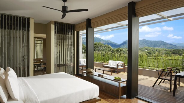 A modern bedroom with a large bed, a ceiling fan, and a balcony with a view of mountains.