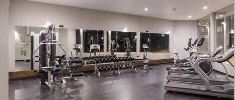 Un gimnasio con diverso equipo de ejercicio, incluyendo cintas de correr y máquinas de pesas, y un espejo grande.