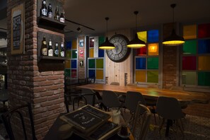 Un restaurante con pared de ladrillo, mesa y sillas de madera. Hay botellas en estantes y un reloj en la pared.