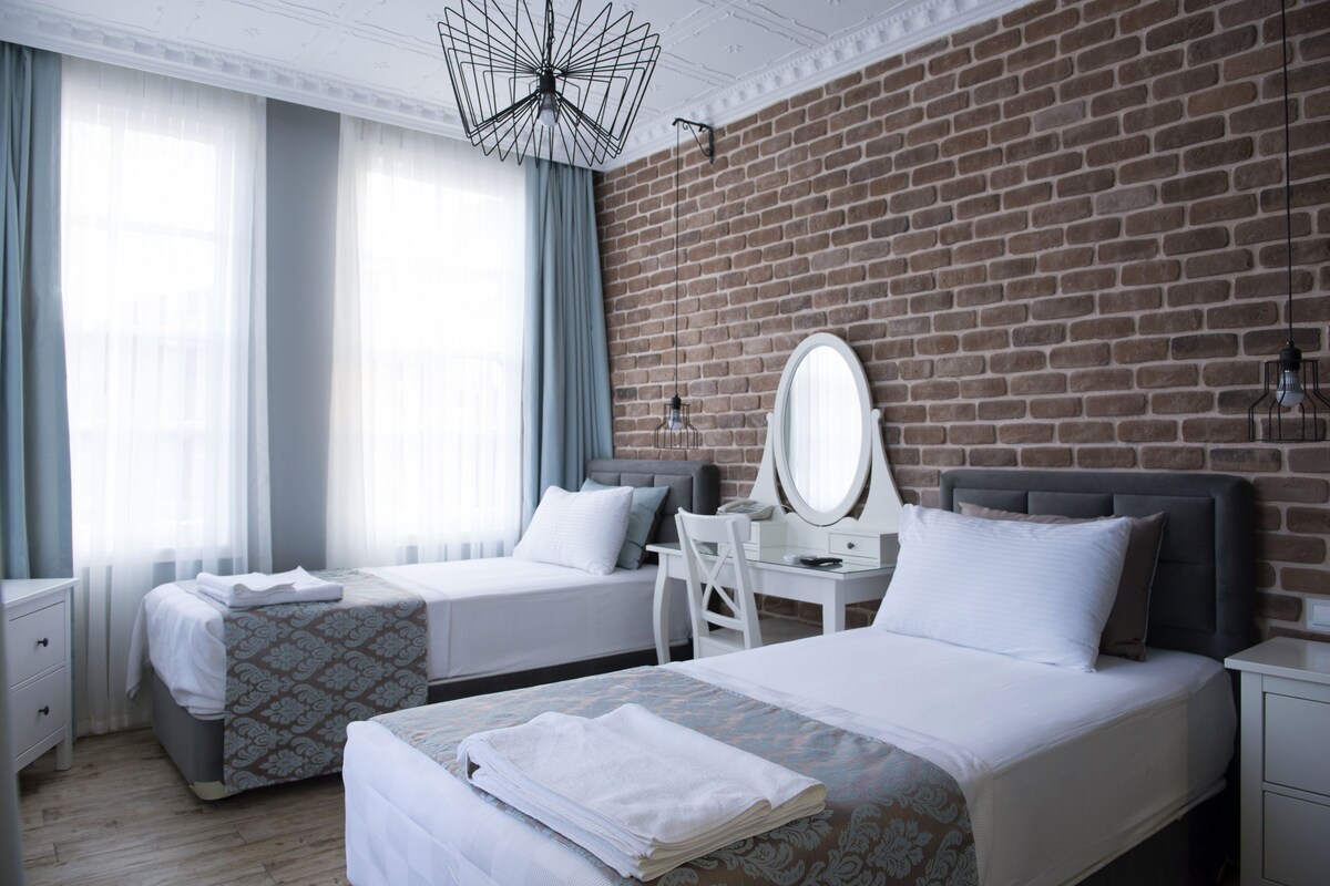 Habitación de hotel con dos camas, un escritorio, una silla, un espejo y una pared de ladrillo.