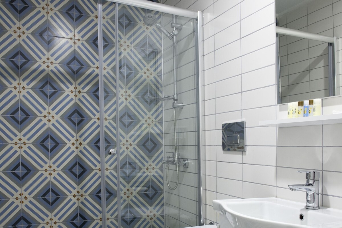 Un baño con piso estampado, cabina de ducha de vidrio, lavamanos blanco y un inodoro.