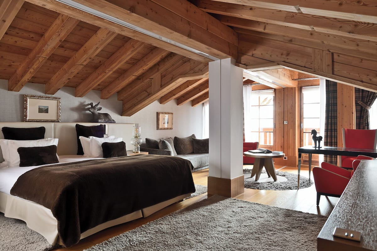 A cozy bedroom with a wooden ceiling, a large bed with multiple pillows, a small table, and a red chair.