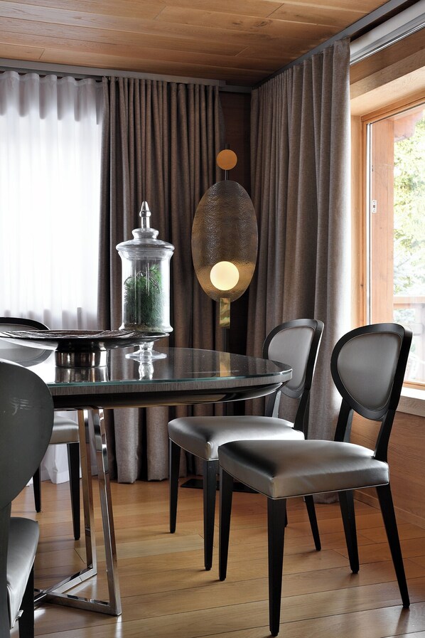A modern dining area with a round glass table, two chairs, a decorative glass jar, and a pendant light.