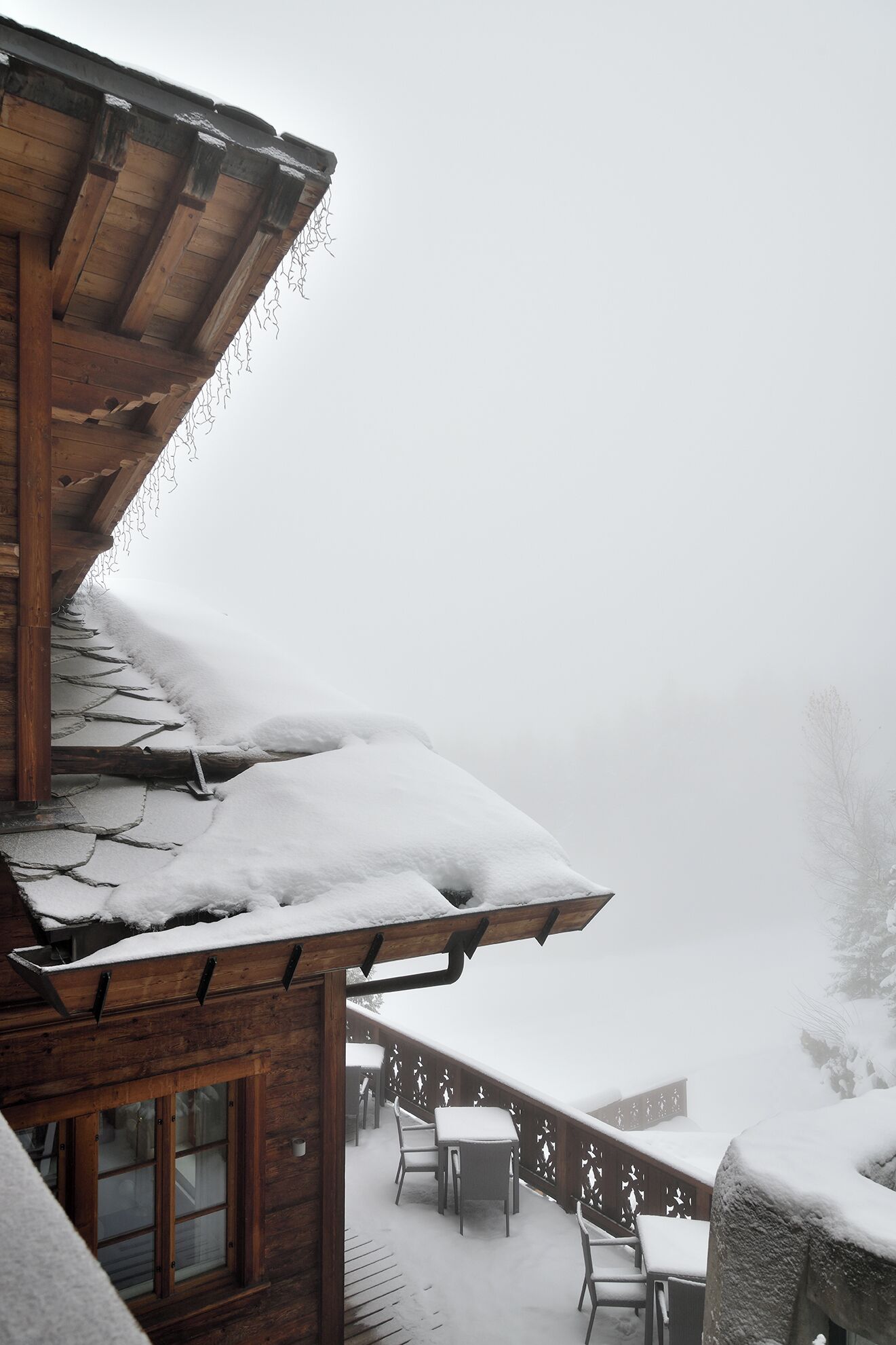 A wooden cabin with a snow-covered roof and balcony.
