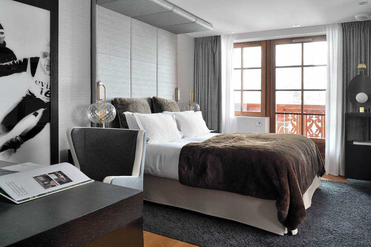 A modern hotel room with a large bed, a desk, and a view of the outdoors.