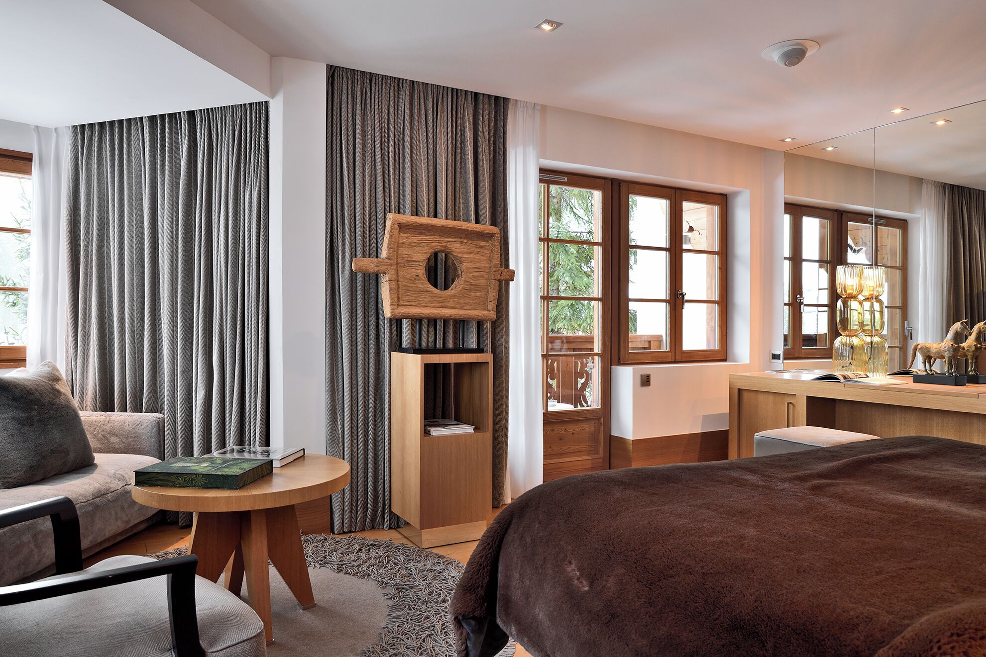 A modern bedroom with a large bed, a wooden desk, and a view of greenery outside.