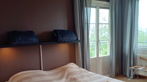 A bedroom with a bed, a bedside table, a hanging light, and a window with curtains.