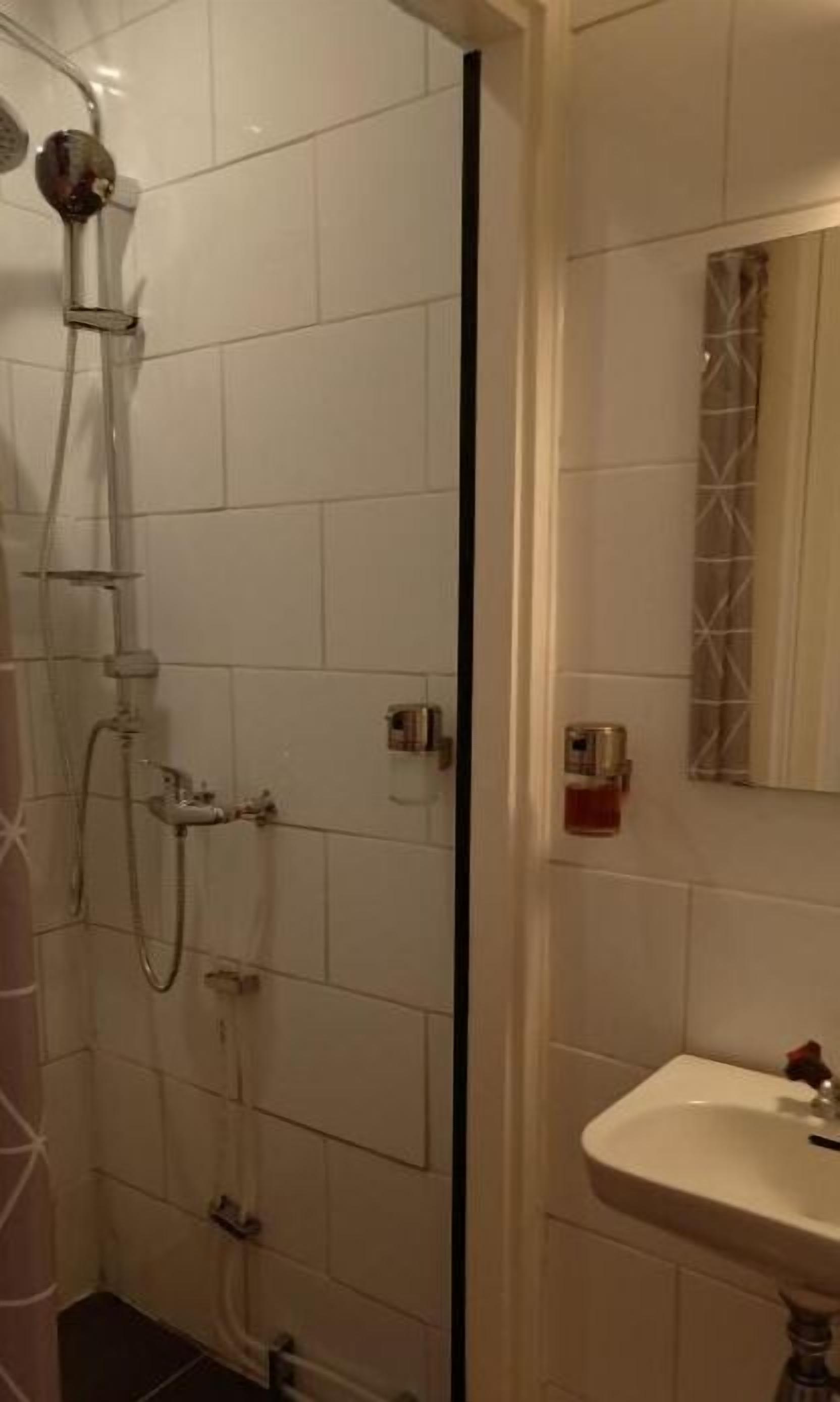 A bathroom with white tiled walls, a shower with a handheld showerhead, a sink with a mirror, and a towel rack.