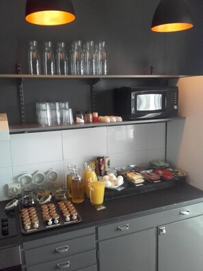 A kitchen with a microwave, shelves with glass bottles, and a variety of food items on the counter.