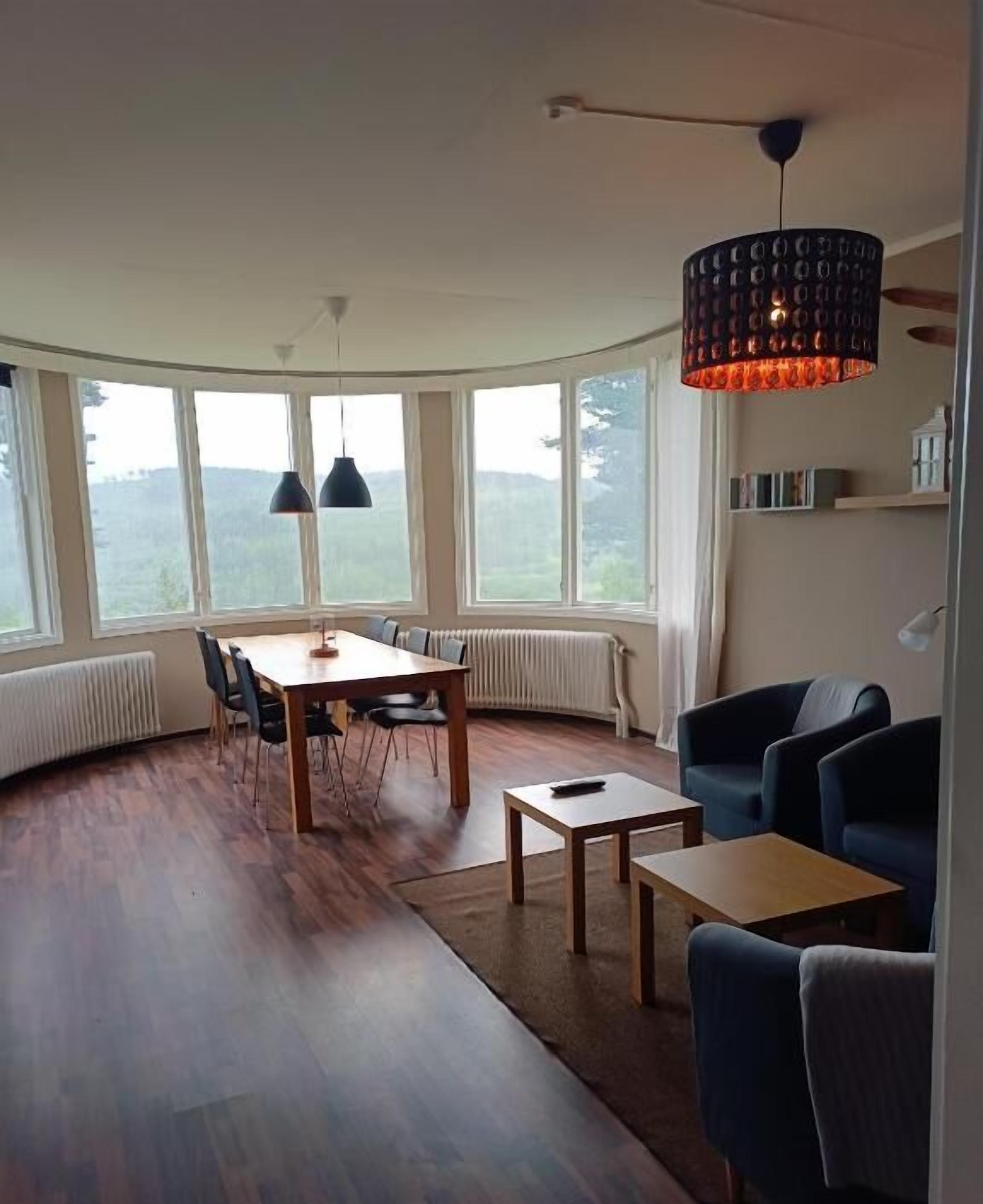 A modern living room with a dining area, large windows, and a unique ceiling light fixture.