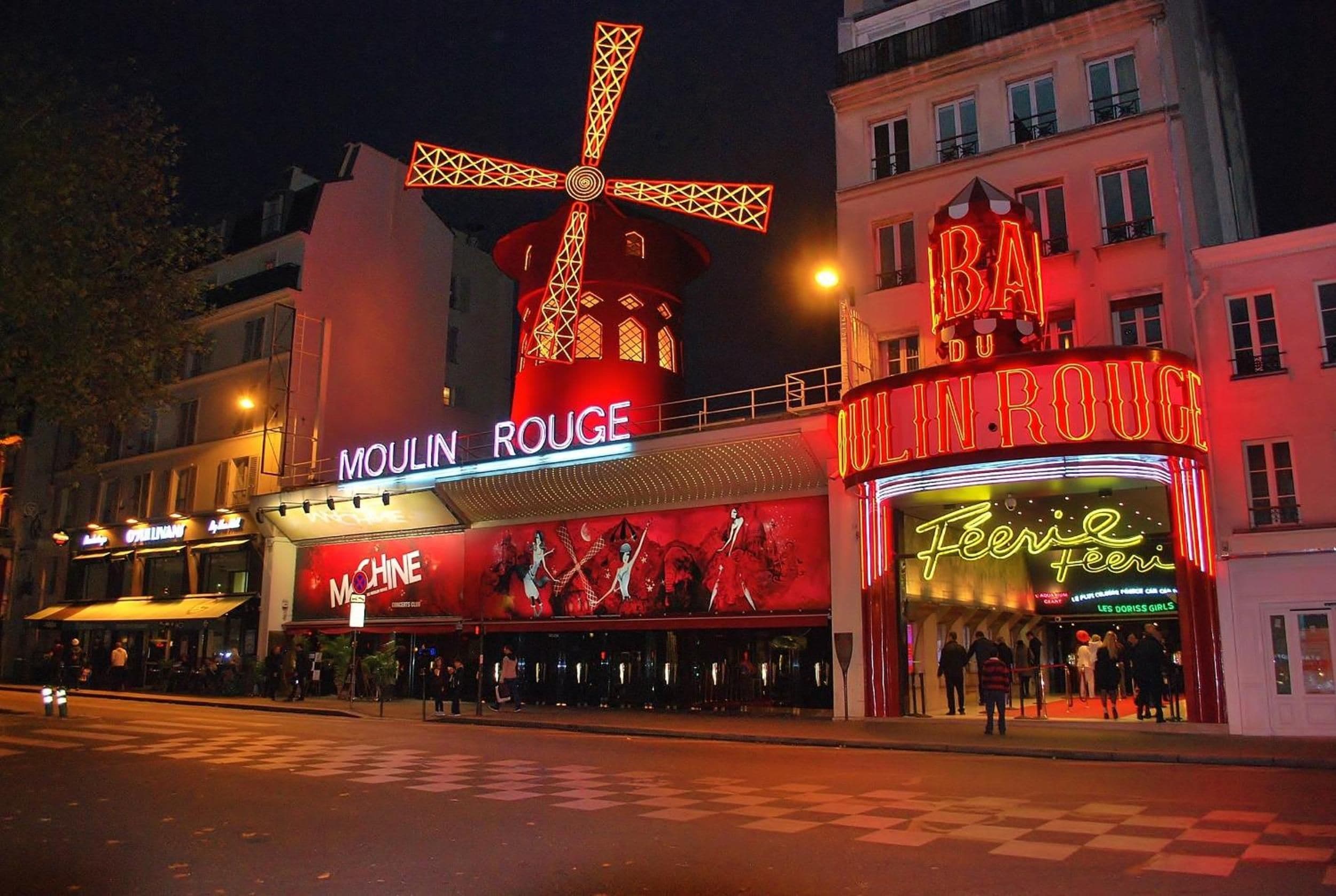 A brightly lit building with illuminated signs for 'Moulin Rouge' and 'Bai Du Roux.'