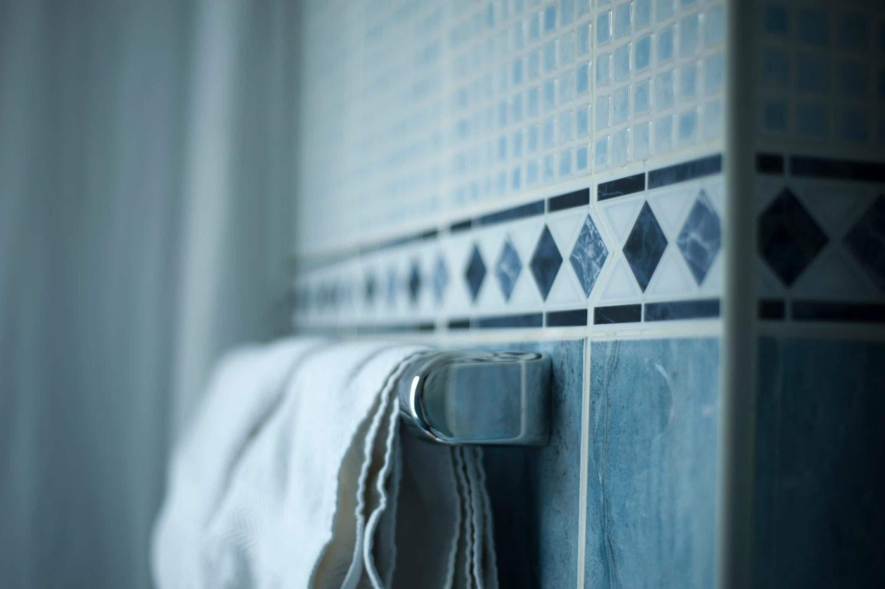 Un baño con pared de azulejos y una toalla colgada en un perchero.