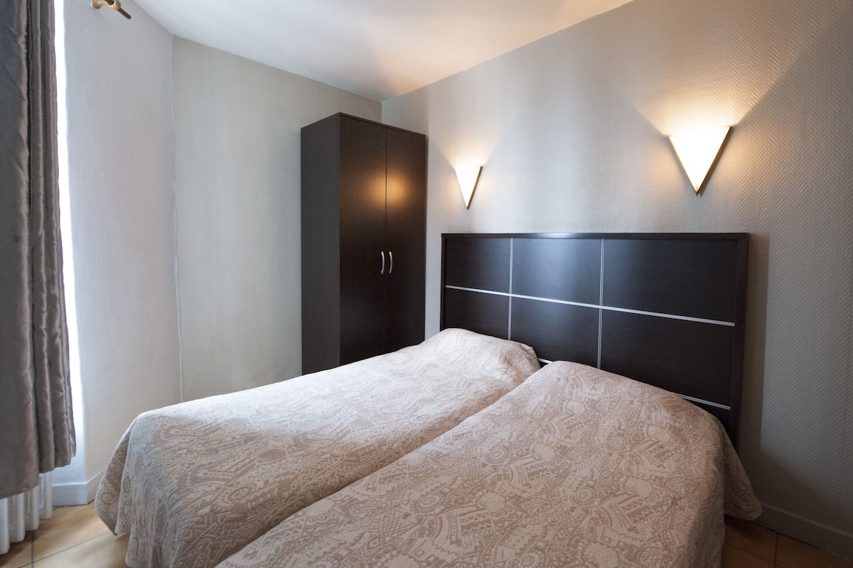 A bedroom with two beds, a wardrobe, and wall-mounted lighting.