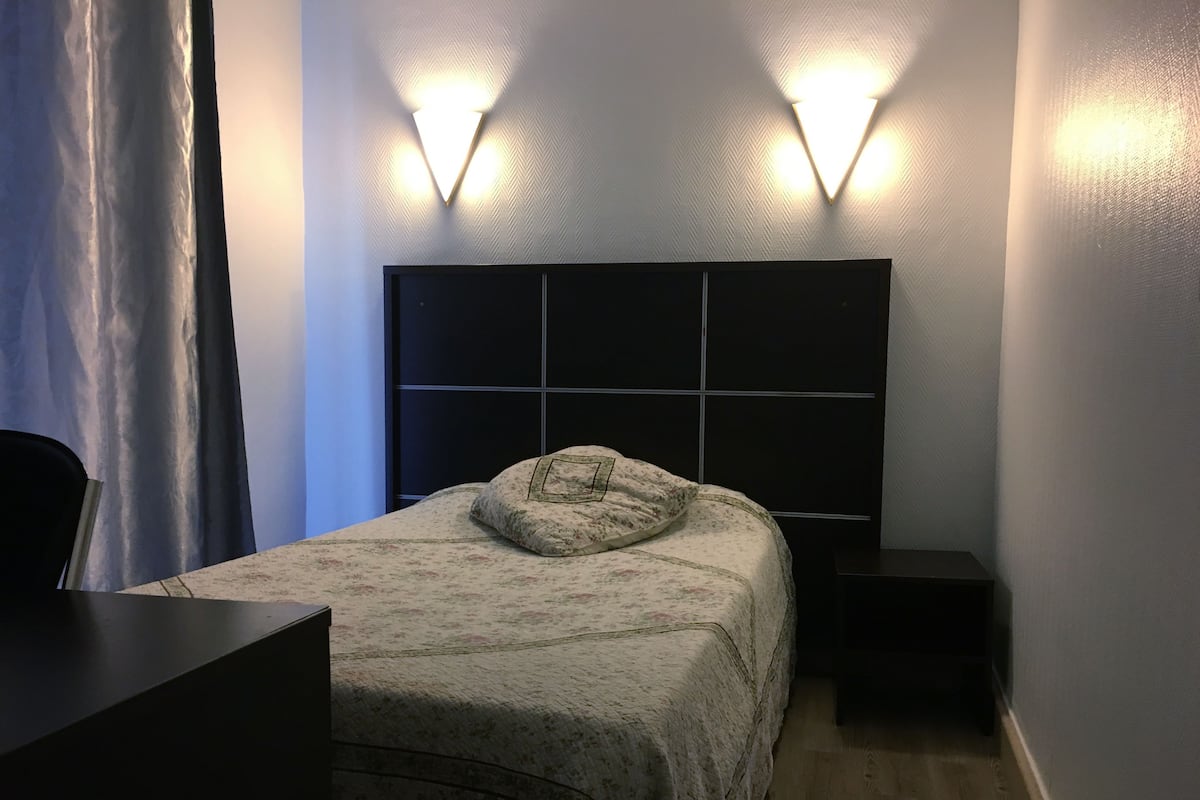 A hotel room with a bed, bedside tables, a desk, and a chair.