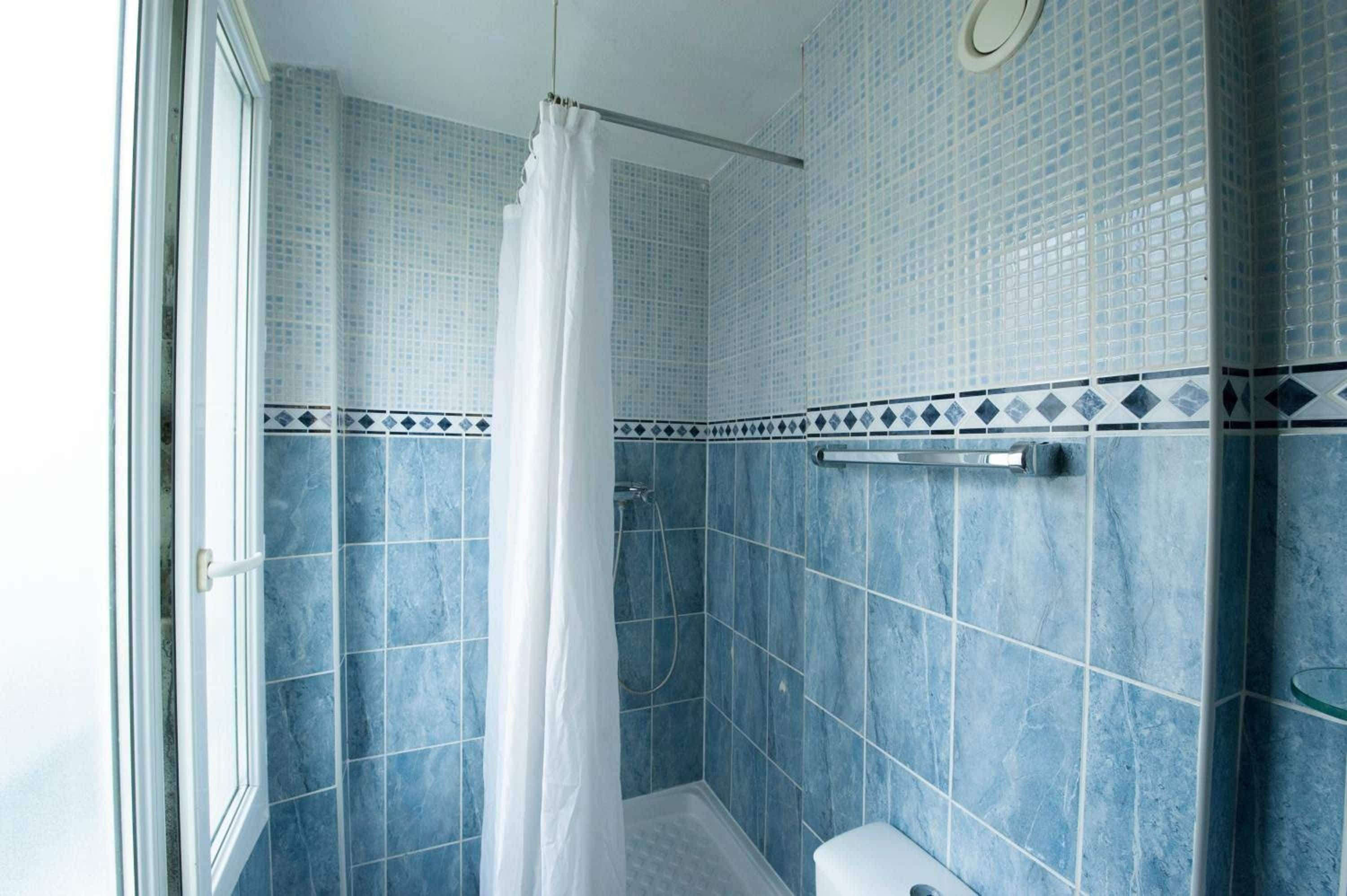 A bathroom with blue tiles, a shower curtain, and a toilet.
