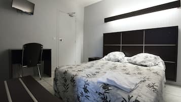 A bedroom with a bed, a desk, a chair, a TV, and a bedside table.
