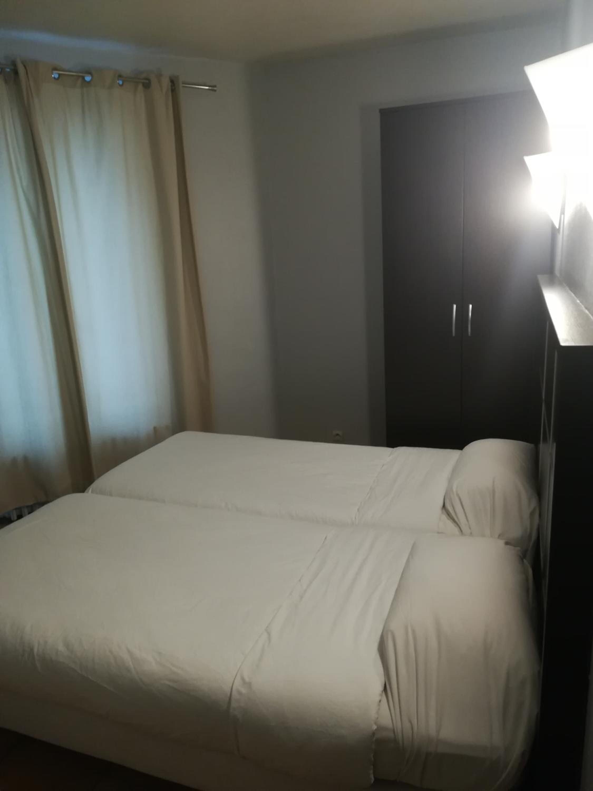 A single bed with a headboard, a dark wardrobe, and a curtain.