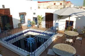 A courtyard with a pool, outdoor seating, and a white building with blue accents.