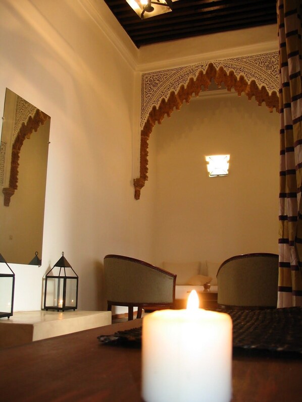 A room with a large mirror, two chairs, a candle, and a decorative arch.