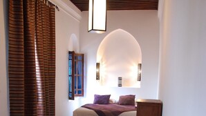 A bedroom with a bed, a wooden headboard, a patterned rug, and a window with curtains. - Riad Dar Soufa (Rabat)