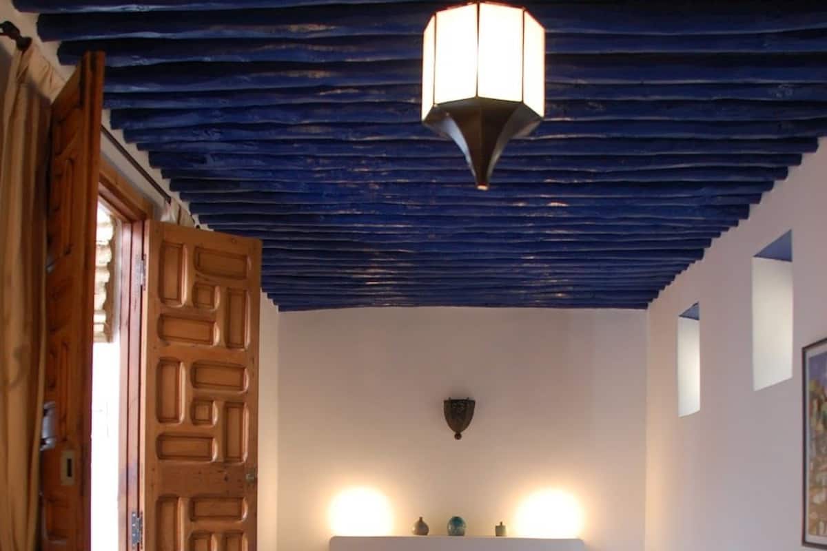 Un dormitorio con cama, puerta de madera, una lámpara en el techo y un pequeño aplique de pared.