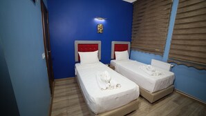 A hotel room with two single beds, a wooden floor, a blue wall, and a window with blinds. - Taksim Park  (Istanbul)