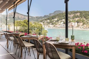 Terraza con mesas preparadas para comer, con vista a un pueblo costero y una playa.