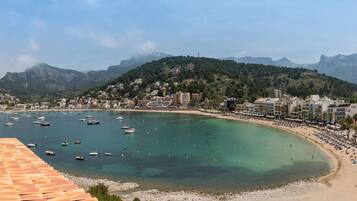 A coastal town with a beach, boats, and mountains in the background.