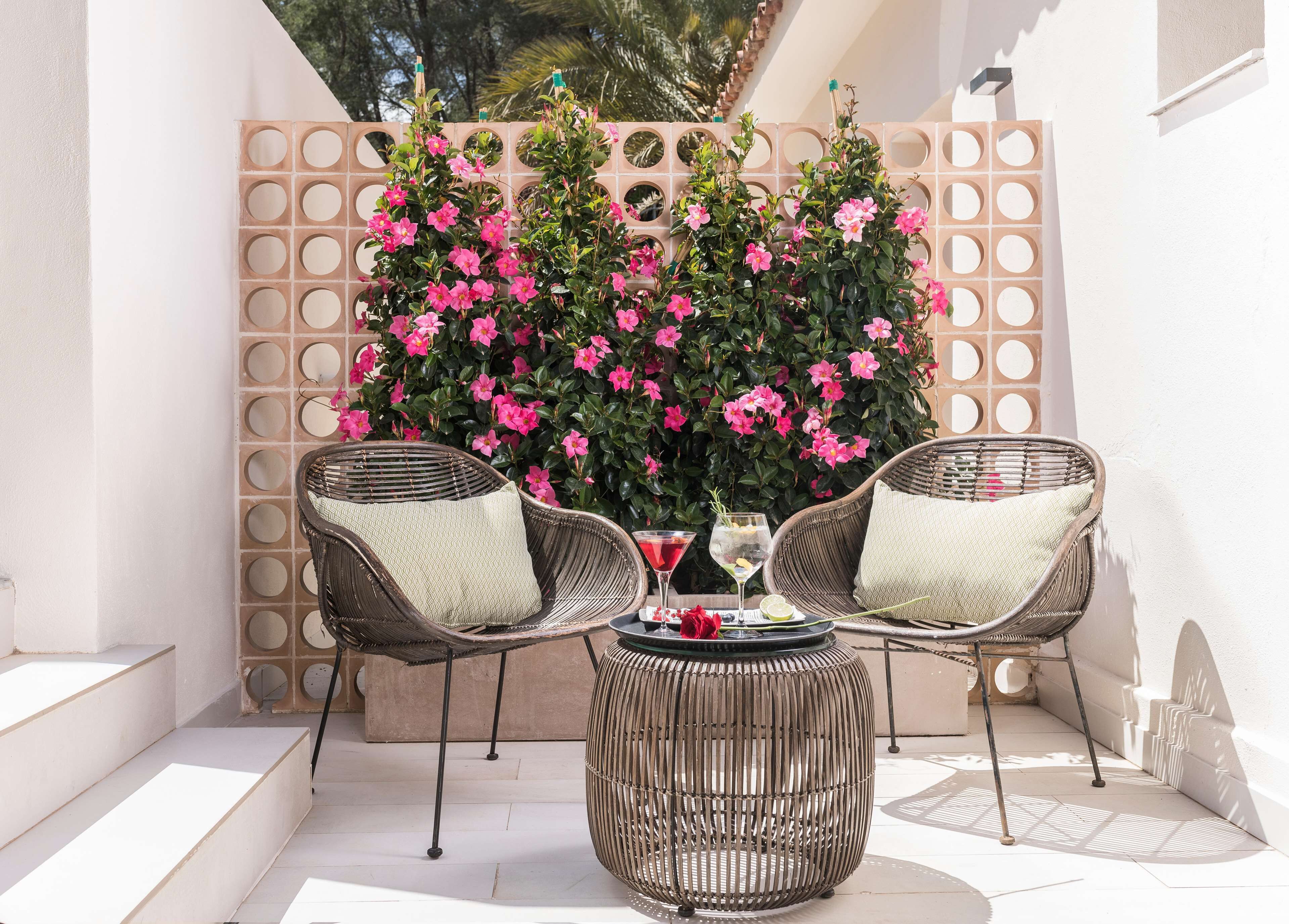 A patio with wicker chairs, a round table, and a backdrop of pink flowers.