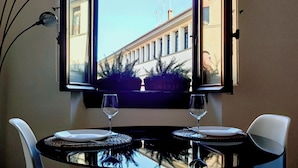 A corner room with a table and chairs, a window with curtains, and a view of a building outside. - My Guest In Florence (Florence)