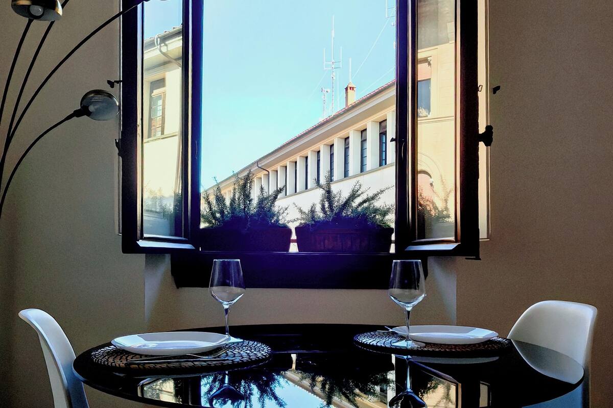 A corner room with a table and chairs, a window with curtains, and a view of a building outside.