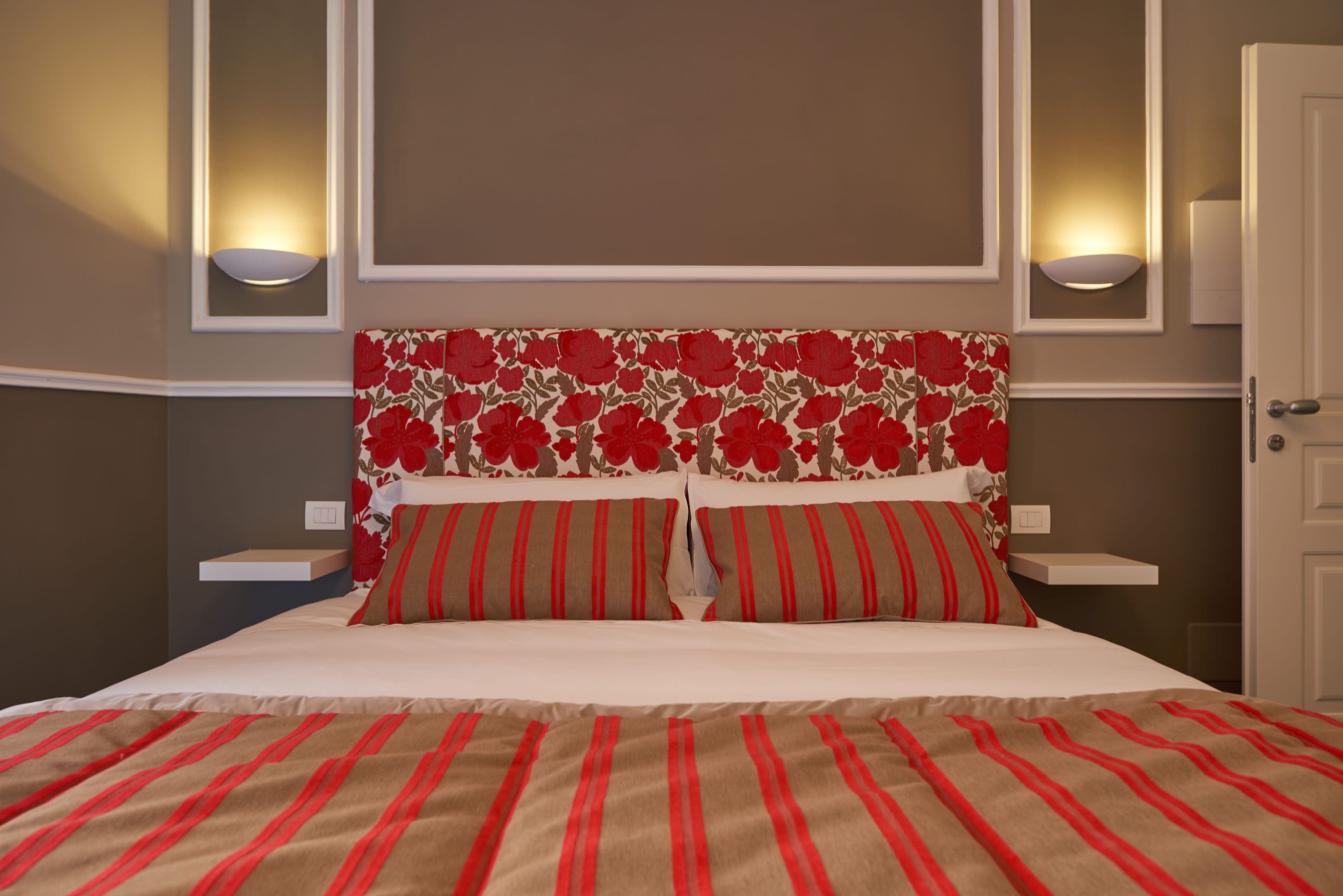 A neatly made bed with striped bedding, a floral headboard, and two wall-mounted lamps.