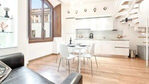 A modern kitchen with white cabinets, a dining area with a table and chairs, and a staircase with wooden steps. - My Guest In Florence (Florence)