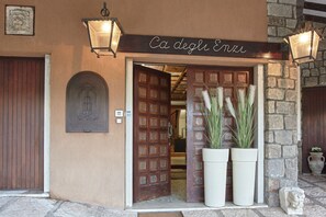 A hotel entrance with a wooden door, a sign reading "Ca degli Enni", and two large potted plants. - Residenza Ca' degli Enzi (Verona)