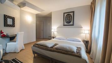 Habitación de hotel con una cama grande, lámparas de noche, una silla, un escritorio y un cuadro en la pared.