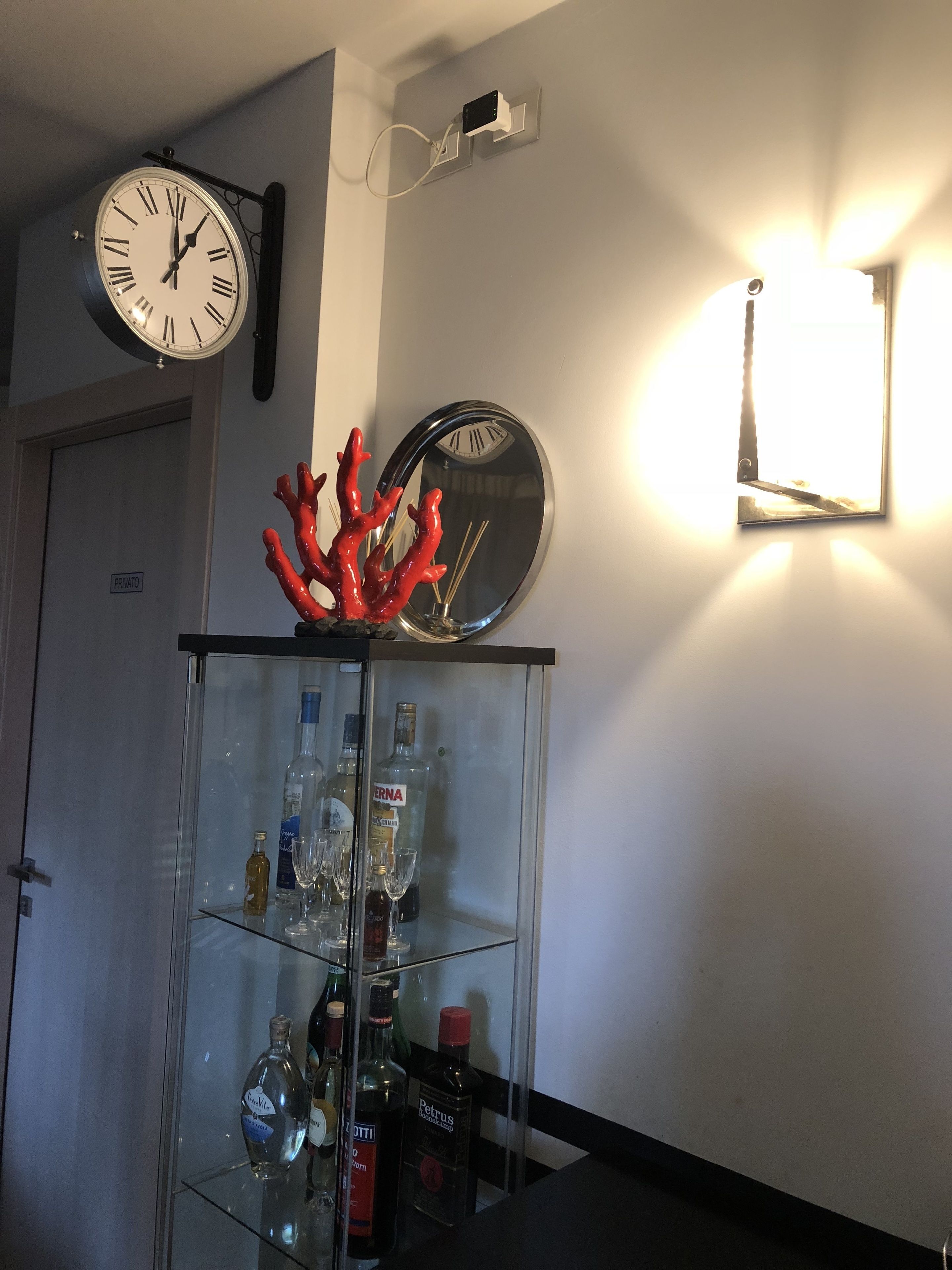 A room with a glass display cabinet containing liquor bottles, a wall clock, and a decorative coral piece.