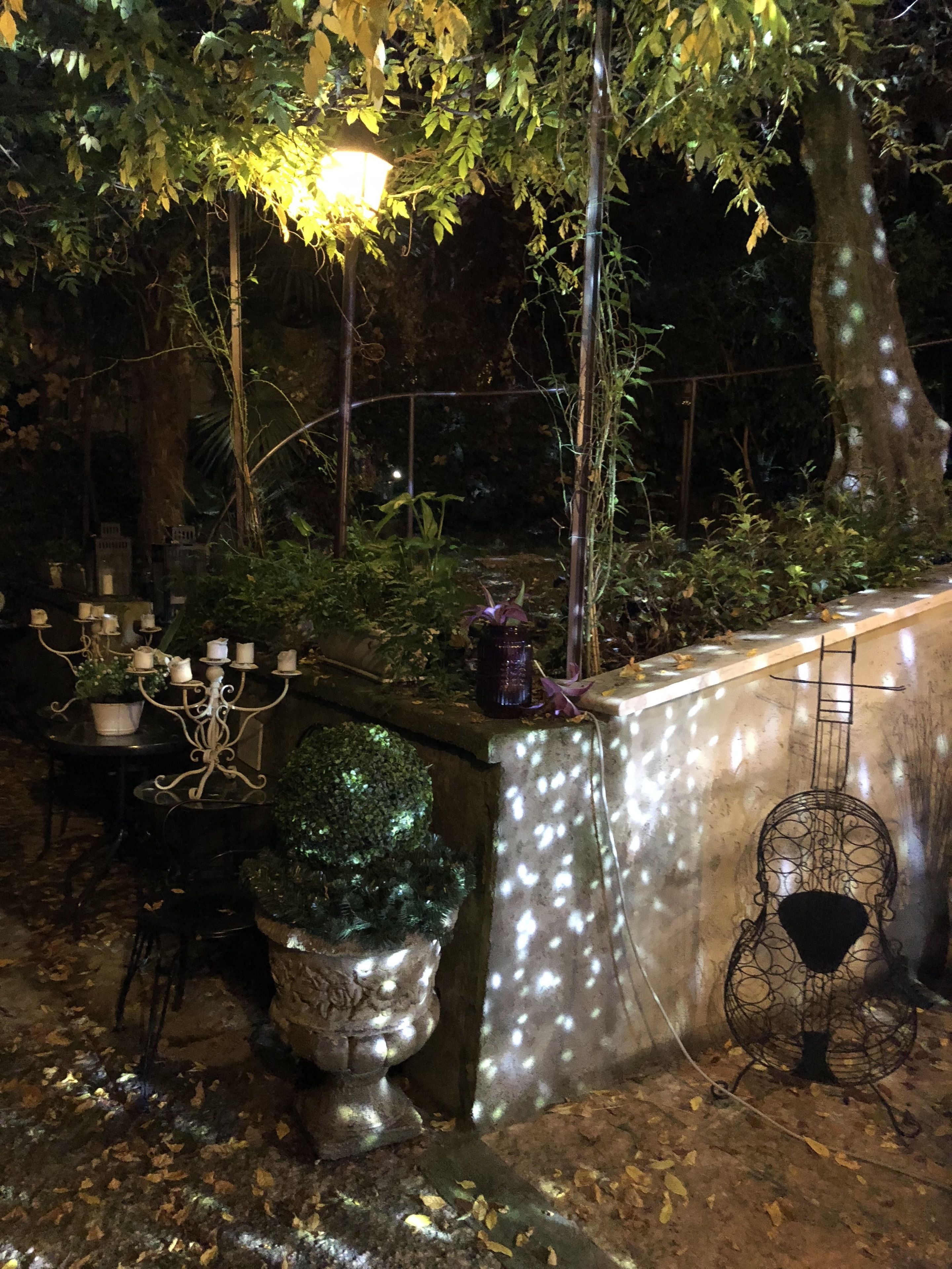 An outdoor garden area with a stone bench, a table with candles, and a decorative plant.