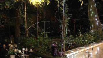 An outdoor garden area with a stone bench, a table with candles, and a decorative plant.