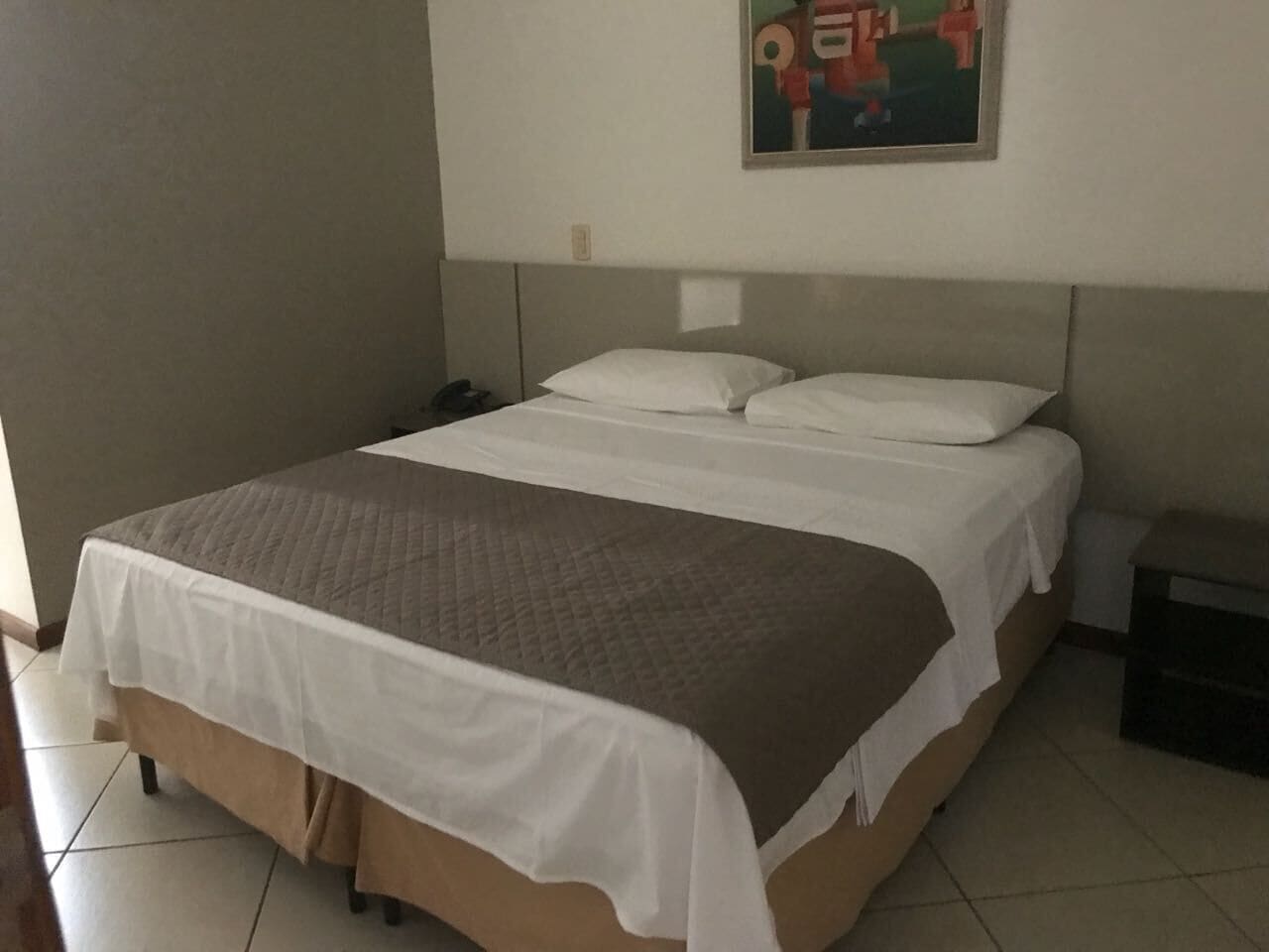 Una cama bien hecha con un edredón blanco y marrón, un cabecero y una mesita de noche pequeña con una lámpara.