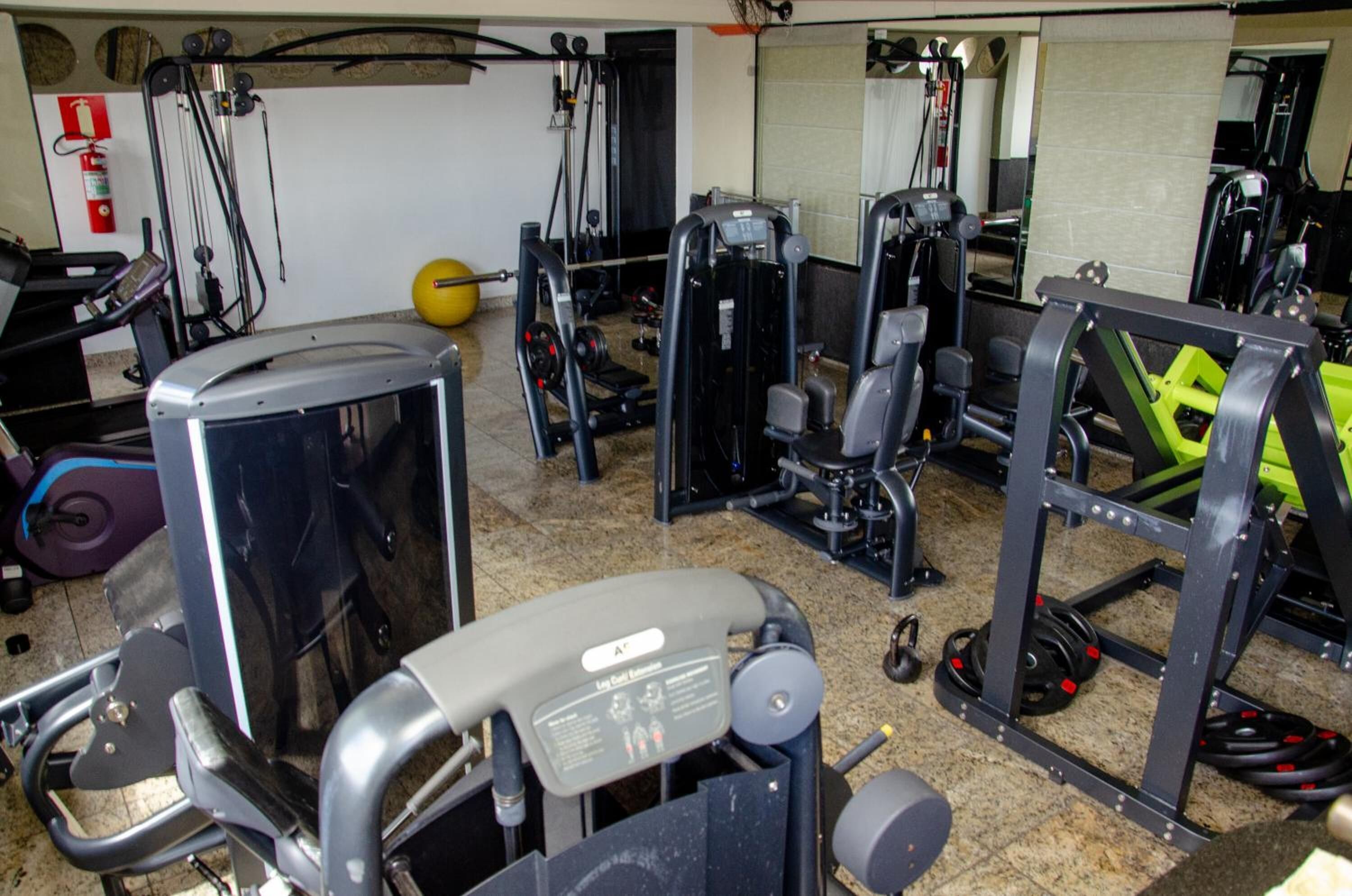 Een sportschool met diverse fitnessapparaten, een brandblusser en een yogabal.