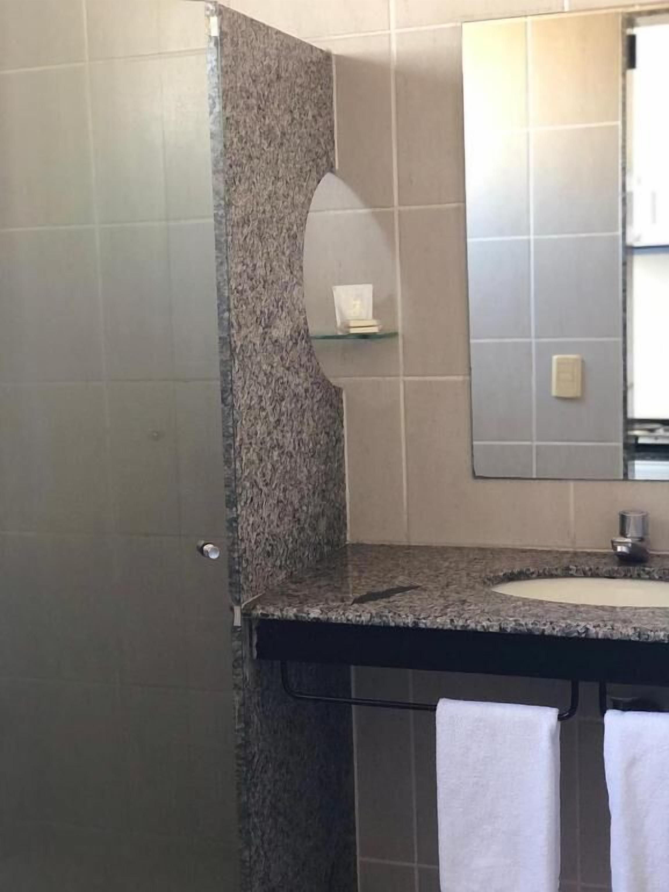 A bathroom with a granite countertop, a sink, a mirror, and a towel rack.