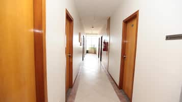 A hallway with wooden doors, a tiled floor, and a sign indicating the direction to the elevator.